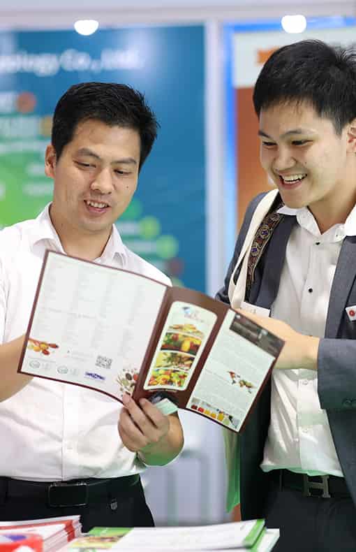 Two attendees at Vitafood Asia smiling while examining a brochure